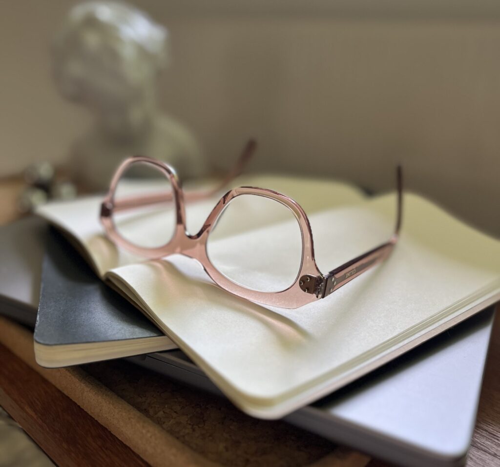 Rosa briller henslengt på toppen av en haug åpne skrivebøker.